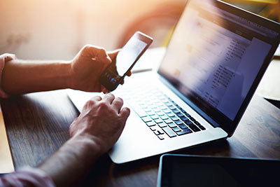 Person holding mobile in front of laptop